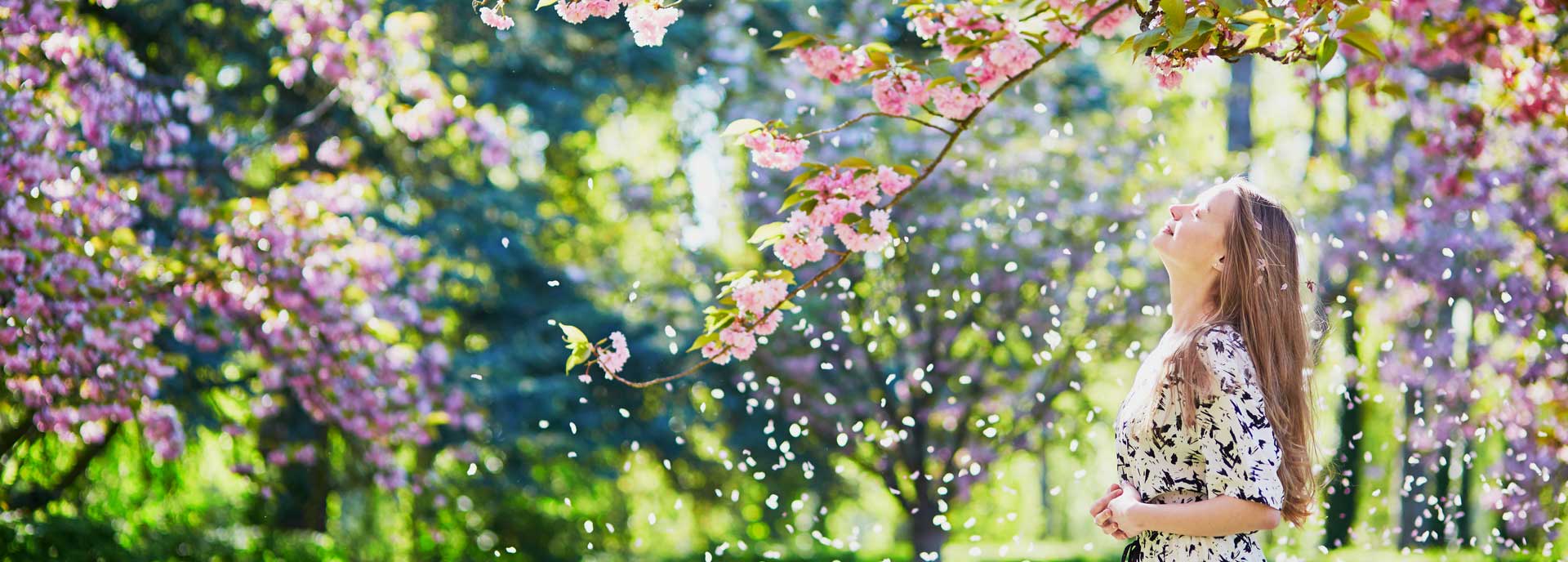 Young woman with head tilted back and standing among flowering trees.