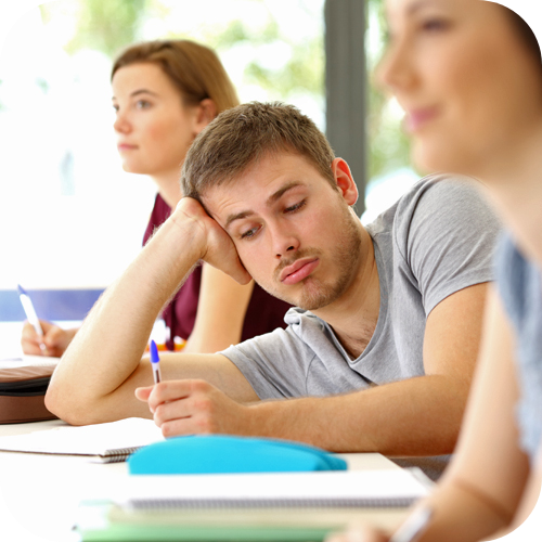 Teenage boy holding his head up at desk in school room, not paying attention.